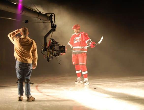 A Carolina Hurricanes player stands in a well-lit space on the floor as a camera aims at him.