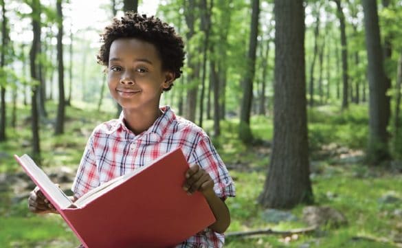 A child runs through a wooded park area with a book in his hands.