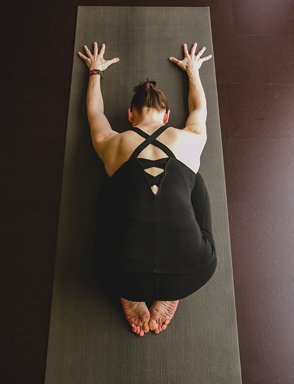 An adult woman rests in child's pose on a yoga mat.